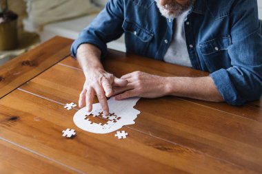 Cropped view of elderly man with alzheimer folding puzzle clipart