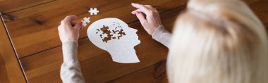 Overhead view of blurred woman holding part of jigsaw on table, banner 