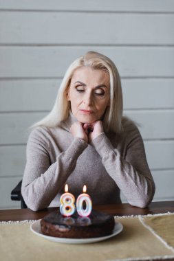 Elderly woman looking at blurred birthday cake on table 