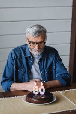 Senior man looking at blurred birthday cake on table 