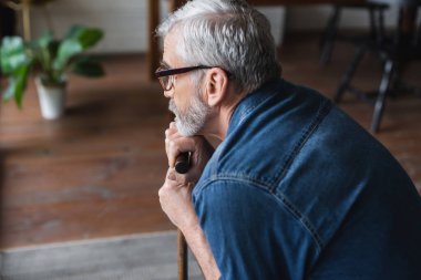 Side view of lonely senior man holding crutch at home 