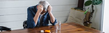 Depressed man looking at pills near glass of water, banner 