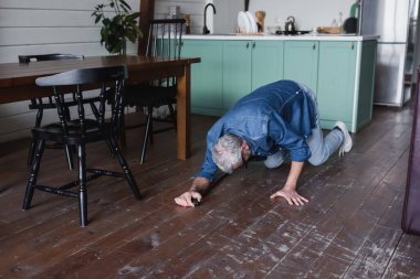 Elderly man with crutch falling on floor in kitchen 