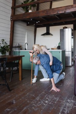 Elderly woman supporting husband with crutch on floor 