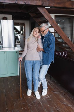 Elderly man helping wife with crutch at home 