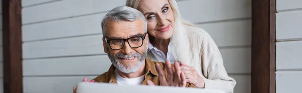 Smiling Senior Man Waving Hand Video Call Blurred Laptop Wife — Stockfoto