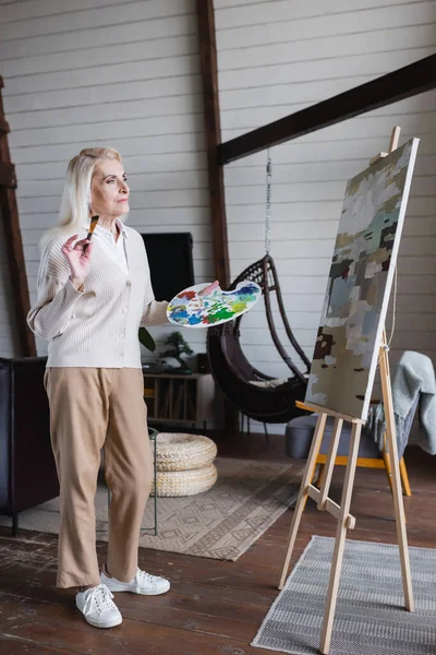 Ältere Frau Mit Pinsel Blickt Auf Leinwand Auf Staffelei — Stockfoto