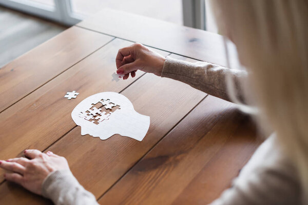Blurred woman folding jigsaw on wooden table 