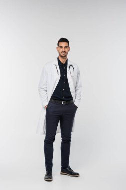 Arap doktor gri arka planda dururken kameraya gülümsüyor