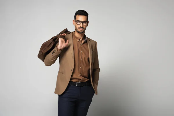 Muslim businessman in eyeglasses holding handbag on grey background