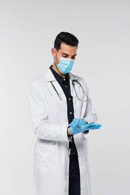 Tıbbi maskeli Müslüman doktor gri eldivenli lateks giyiyor. 