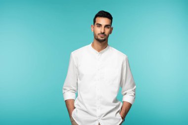 Beyaz gömlekli Müslüman adam mavi kameraya bakıyor. 