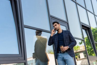 Genç Müslüman işadamı, hazır içecekle dışarıda cep telefonuyla konuşuyor. 