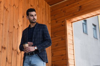 Ceketli genç bir Arap, elinde ahşap cepheli bir içecek tutuyor. 