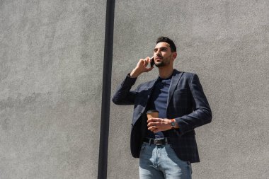 Genç Müslüman menajer cep telefonuyla konuşuyor ve dışarıda yemek fincanı tutuyor. 