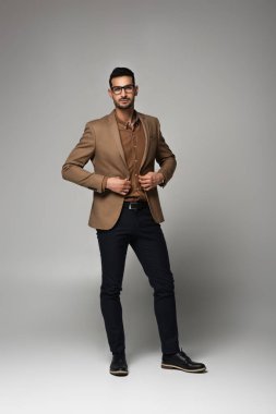 Arap işadamı ceketi düzeltiyor ve gri arkaplandaki kameraya bakıyor