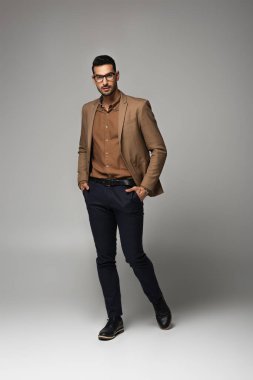 İyi görünümlü Arap işadamı kameraya bakıyor ve gri arka planda yürüyor. 