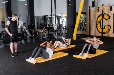 Antrenör kas egzersizi yapan çok ırklı bir grubun yakınındaki fitness izleyicisine bakıyor 