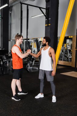 Gülümseyen Afrikalı Amerikalı antrenör spor salonunda sporcuyla el sıkışıyor.