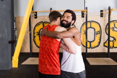 Mutlu Afrikalı Amerikalı antrenör spor salonundaki genç sporcuyu kucaklıyor.