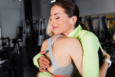 Spor salonundaki sporcuyu kucaklayan gözleri kapalı mutlu bir antrenör.