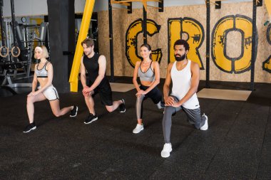 Gülümseyen ırklar arası insanlar spor salonunda ileri atlama egzersizi yapıyorlar.