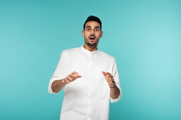 Испуганный мусульманин смотрит на камеру, изолированную на голубом 