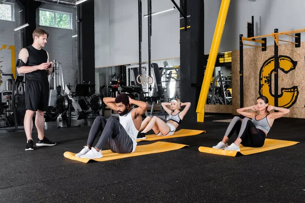 Młody Trener Gospodarstwa Fitness Tracker Pobliżu Międzyrasowe Sportowe Ludzie Robi — Zdjęcie stockowe