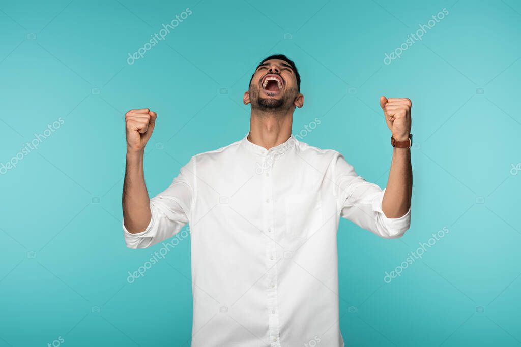 Excited muslim man with closed eyes showing yes gesture isolated on blue 