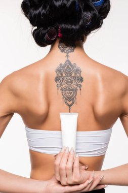 back view of young woman in curlers with tattoo holding cream tube isolated on white clipart