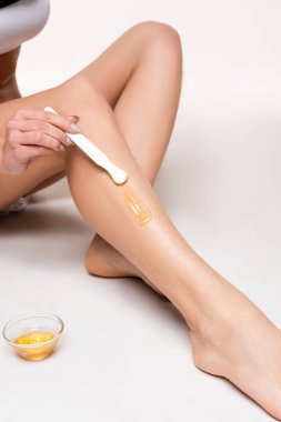 partial view of young woman making epilation on leg near bowl with honey on white clipart