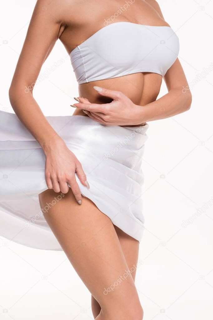 partial view of silk cloth covering hips of young woman with hands near body isolated on white