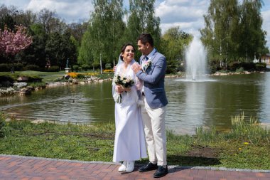 Neşeli gelin ve damat parkta çeşmenin yanında duruyor. 