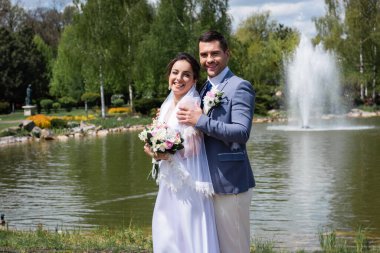Parktaki bulanık çeşmenin yanında duran mutlu gelin ve damat 