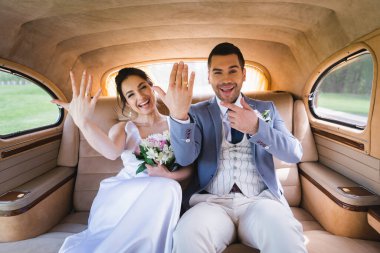 Neşeli damat, retro otomobilde gelinin yanındaki yüzüğü işaret ediyor. 
