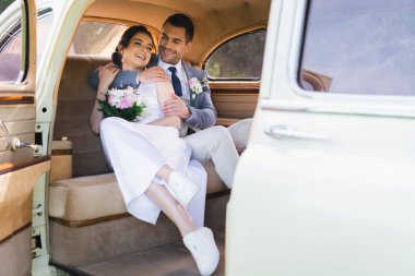 Smiling groom embracing bride in vintage car  clipart