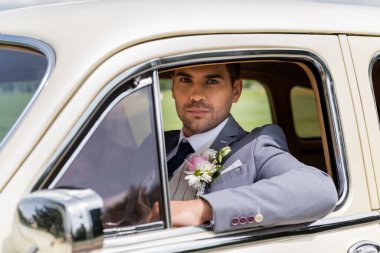 Seçkin damat klasik arabadaki kameraya bakıyor. 
