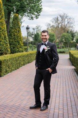 Gülümseyen damat parkta el ele tutuşuyor. 