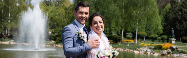Веселые молодожены смотрят в камеру в парке, баннер 