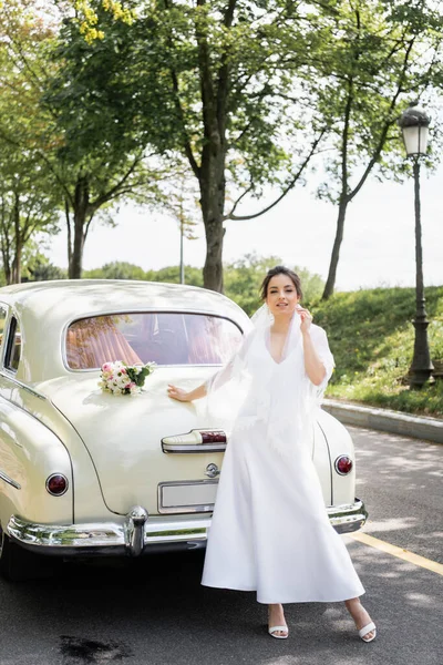 微笑的新娘看着路边老式汽车旁边的相机 — 图库照片