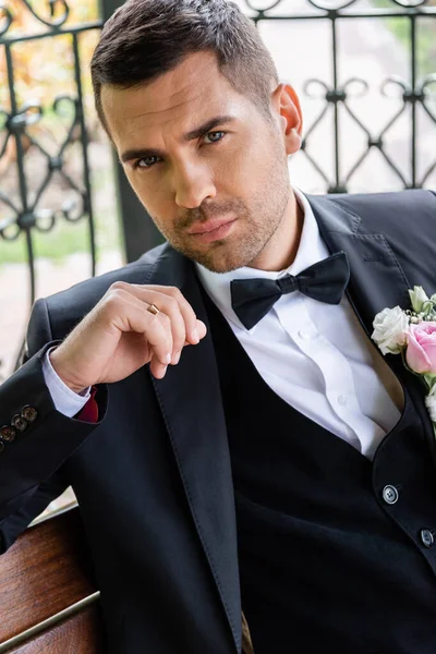 Groom in suit looking at camera on bench in patio outdoors