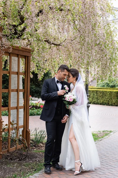 Vista Lateral Jóvenes Recién Casados Parados Cerca Árbol Floreciente Parque —  Fotos de Stock