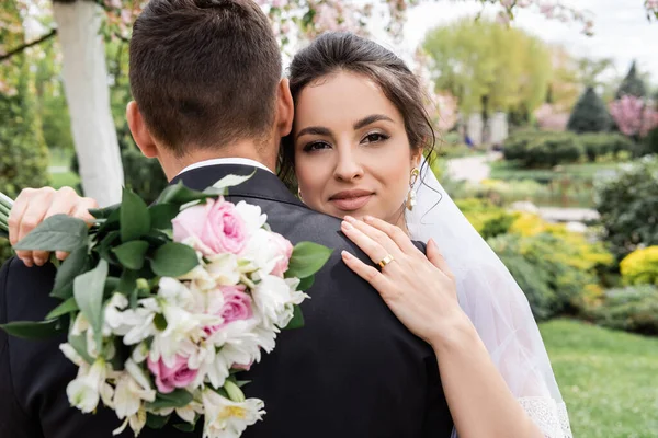 Glimlachende Bruid Met Wazig Boeket Knuffelende Bruidegom Park — Stockfoto