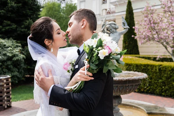 Vista Lateral Recém Casados Com Buquê Beijando Perto Fonte — Fotografia de Stock