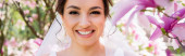 Mladá brunetka nevěsta v závoji při pohledu na kameru poblíž kvetoucí magnólie, prapor 