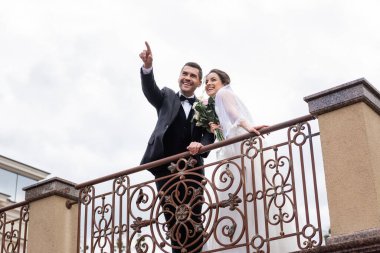 Düşük açılı bakış açısıyla olumlu damat köprünün yanındaki neşeli gelini işaret ediyor. 