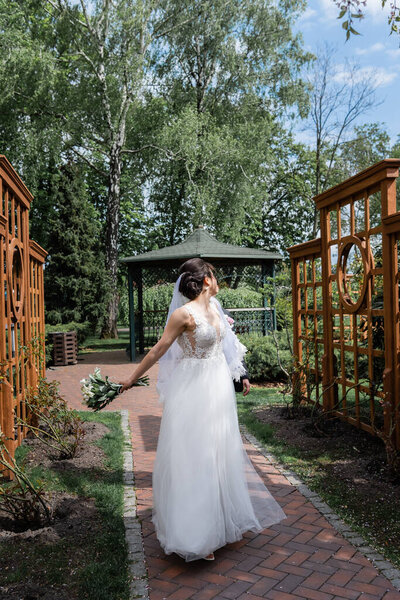 Young bride with bouquet walking near groom in park 