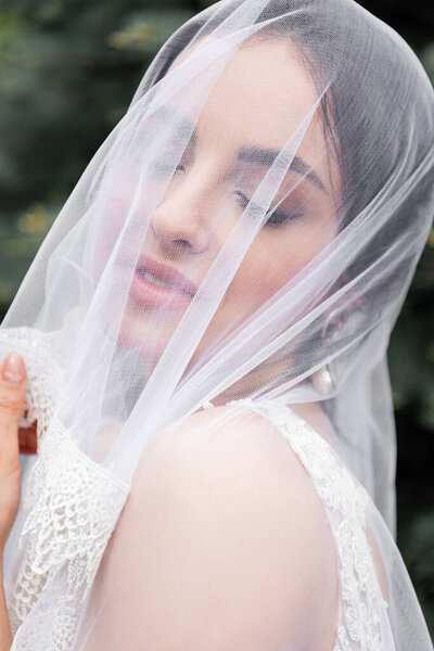 Smiling bride in white veil standing with closed eyes 