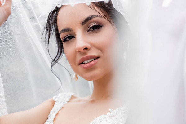 Young bride in wedding dress holding blurred veil 