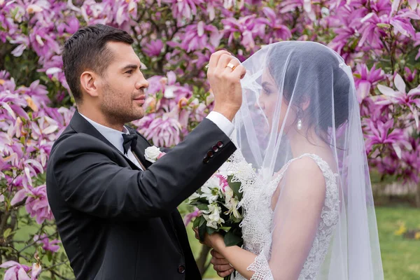 Zijaanzicht Van Bruidegom Opstijgen Sluier Van Bruid Met Boeket Park — Stockfoto